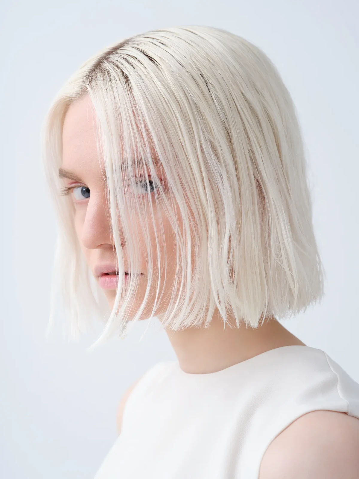 Blonde model with a short bob wearing a white top against a pale studio background