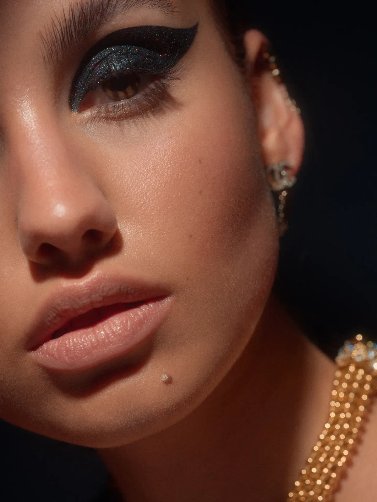 Close beauty portrait with dramatic black eye makeup and gold jewelry in angled light