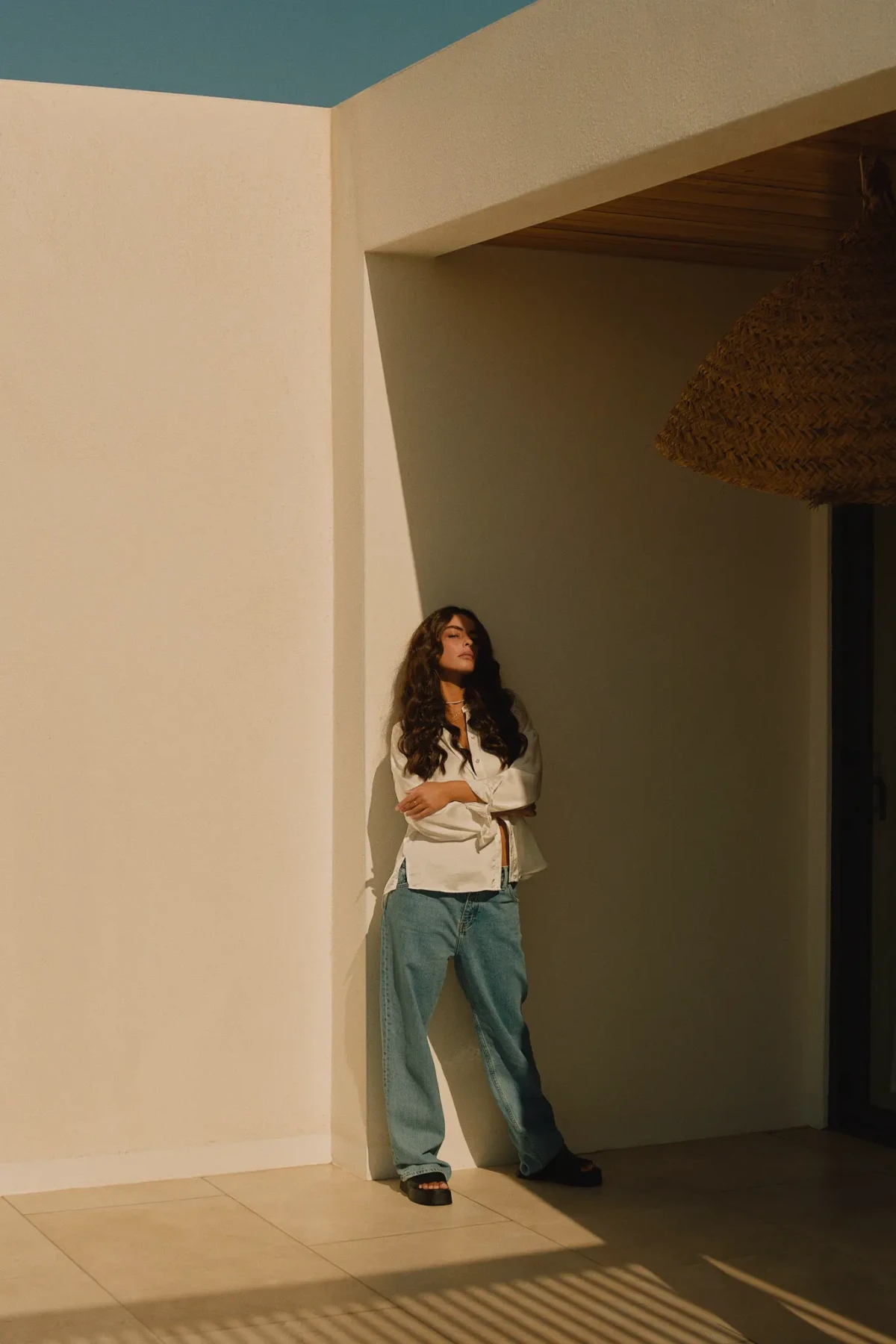 Model in a white shirt and blue trousers standing beside sunlit geometric architecture