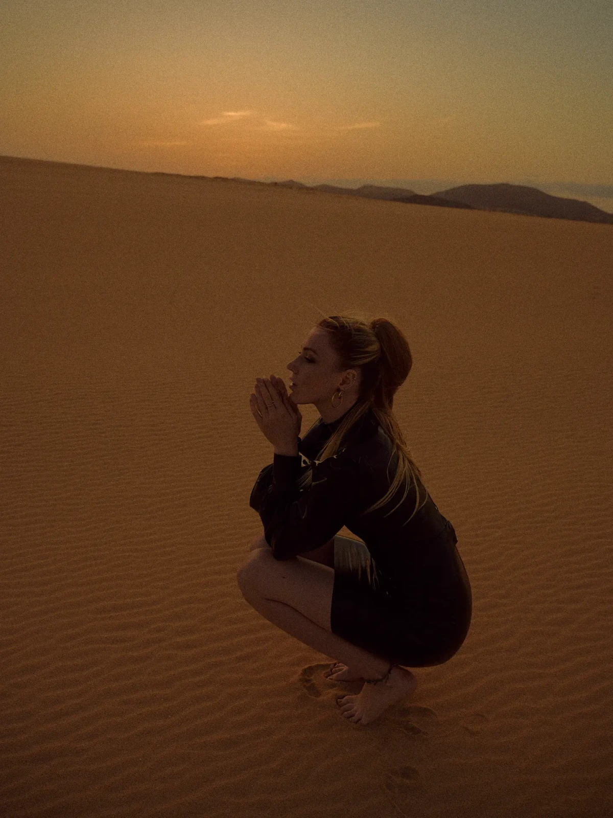 Model crouching on a sand dune in warm sunset light