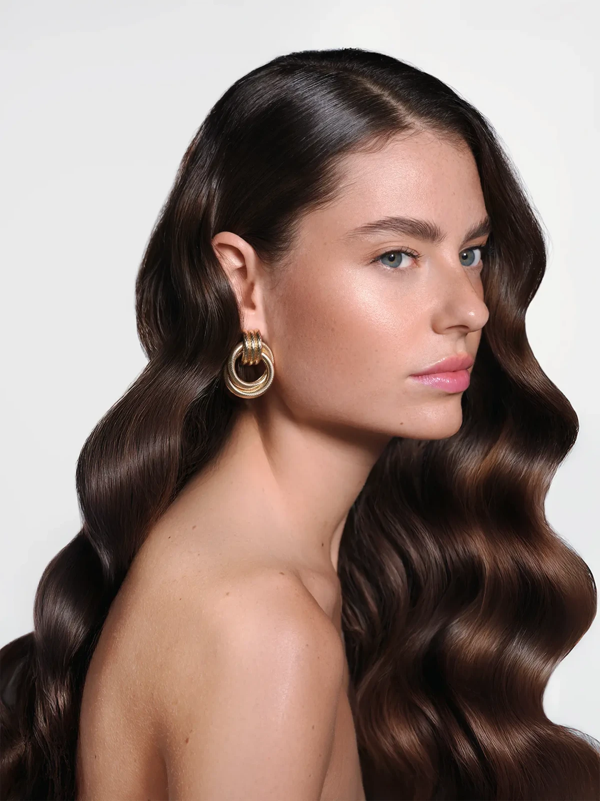 Studio beauty portrait of a brunette model with long glossy waves and gold hoop earrings