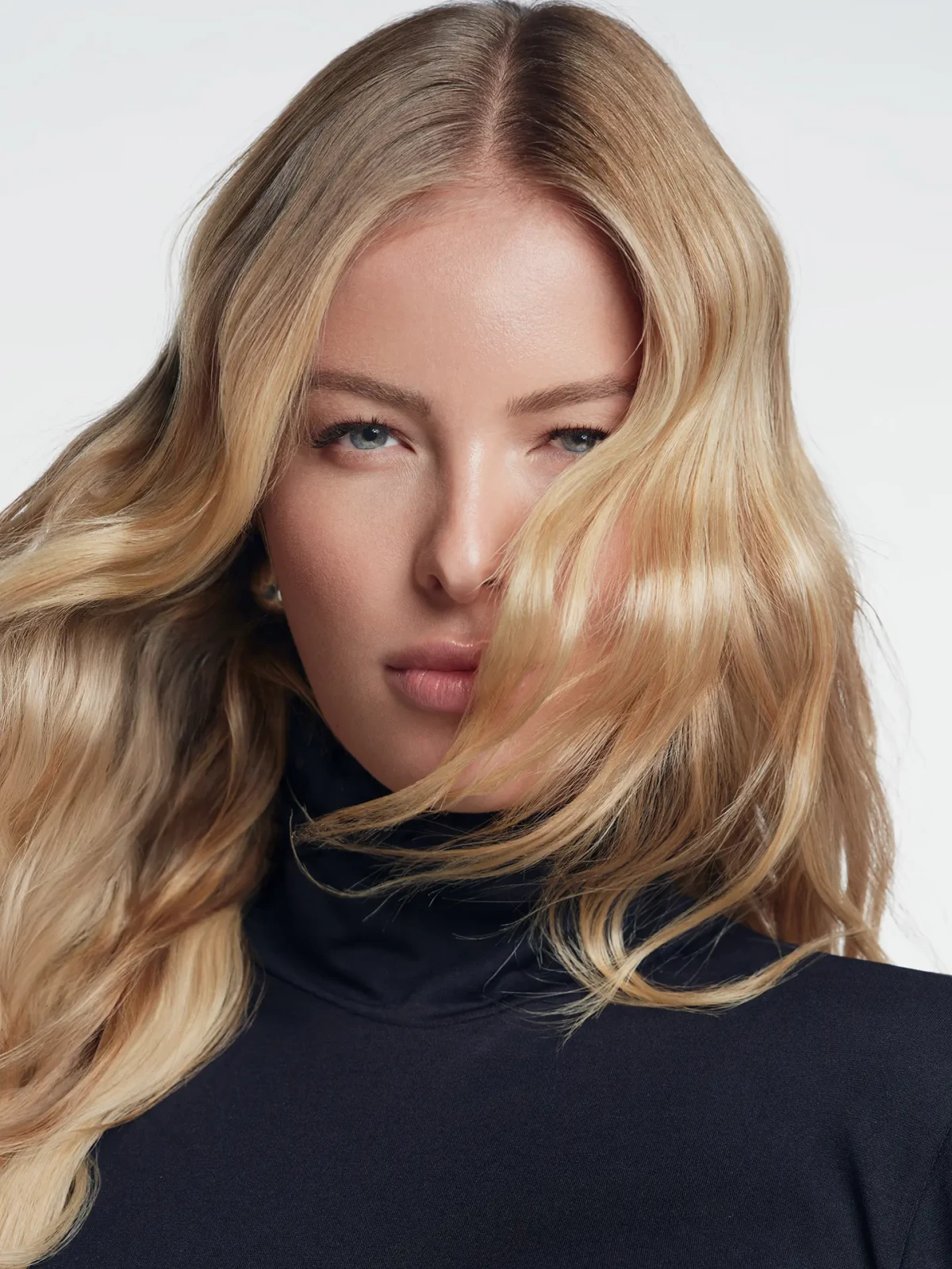 Blonde model with loose wavy hair partially covering her face and a black high-neck top