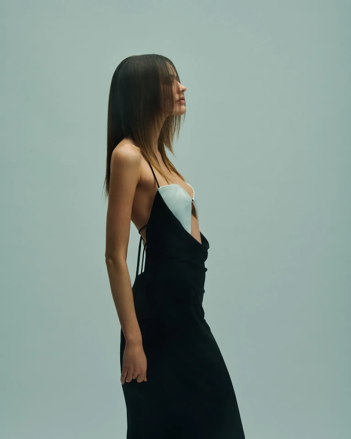 Model in a black dress with straight dark hair against a muted green studio background