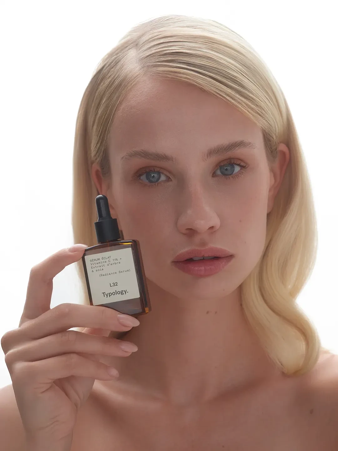 Blonde model holding a Typology skincare bottle beside her face