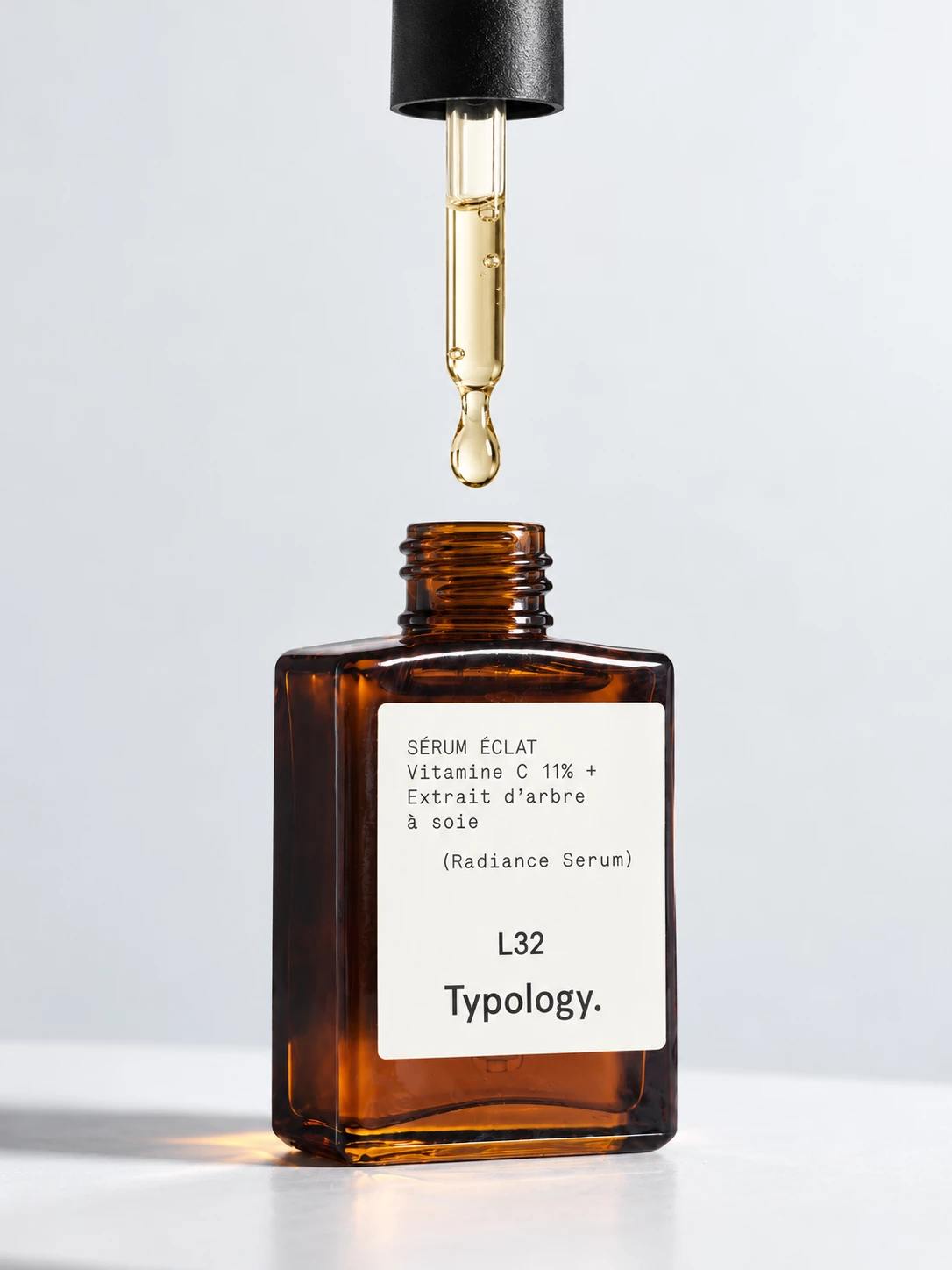 Typology radiance serum bottle with a golden drop falling from a pipette