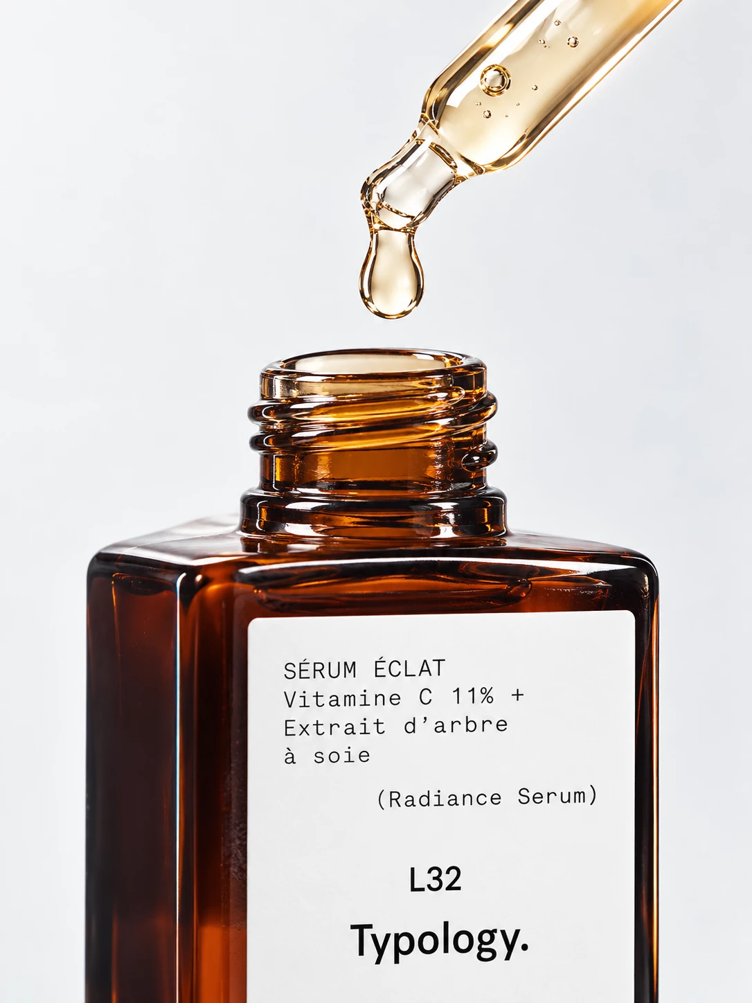 Close-up of a golden serum drop above an open Typology bottle