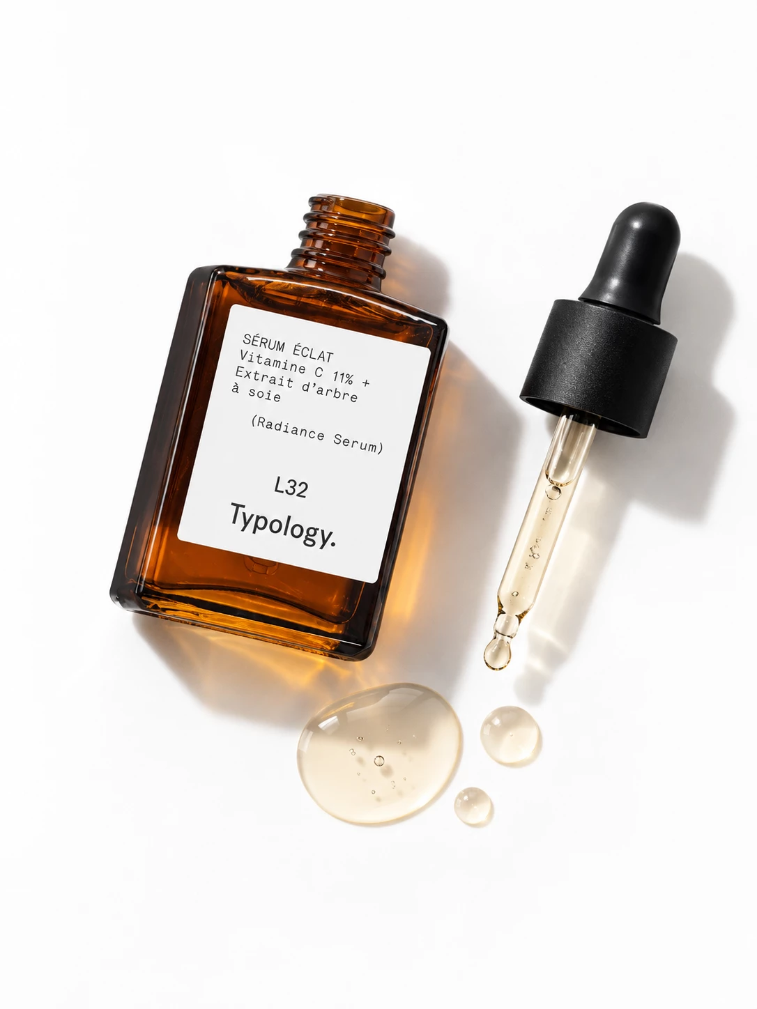 Typology radiance serum bottle, pipette and serum droplets on a white surface