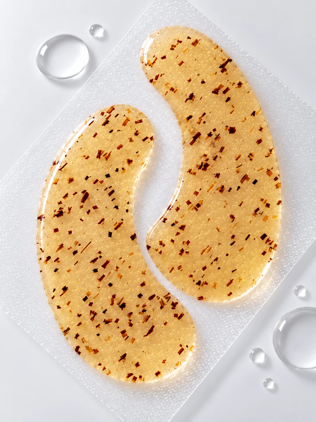 Close-up of golden KAZ Beauty eye pads on textured glass with water droplets