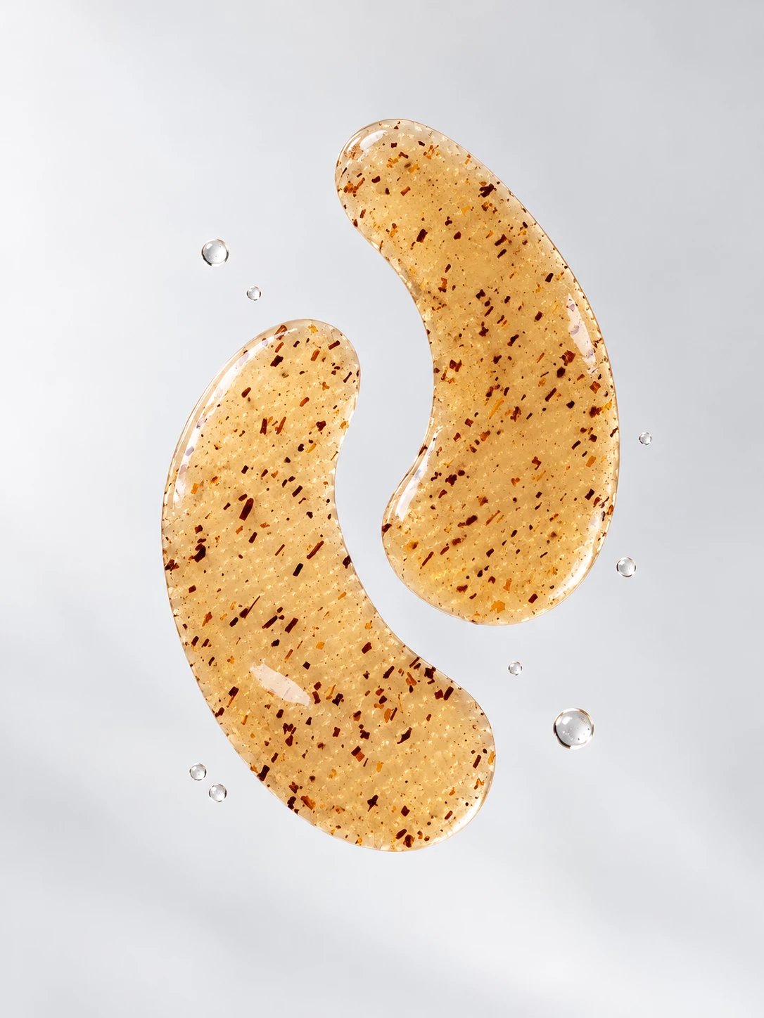 Golden KAZ Beauty eye pads suspended against a soft grey background with water droplets