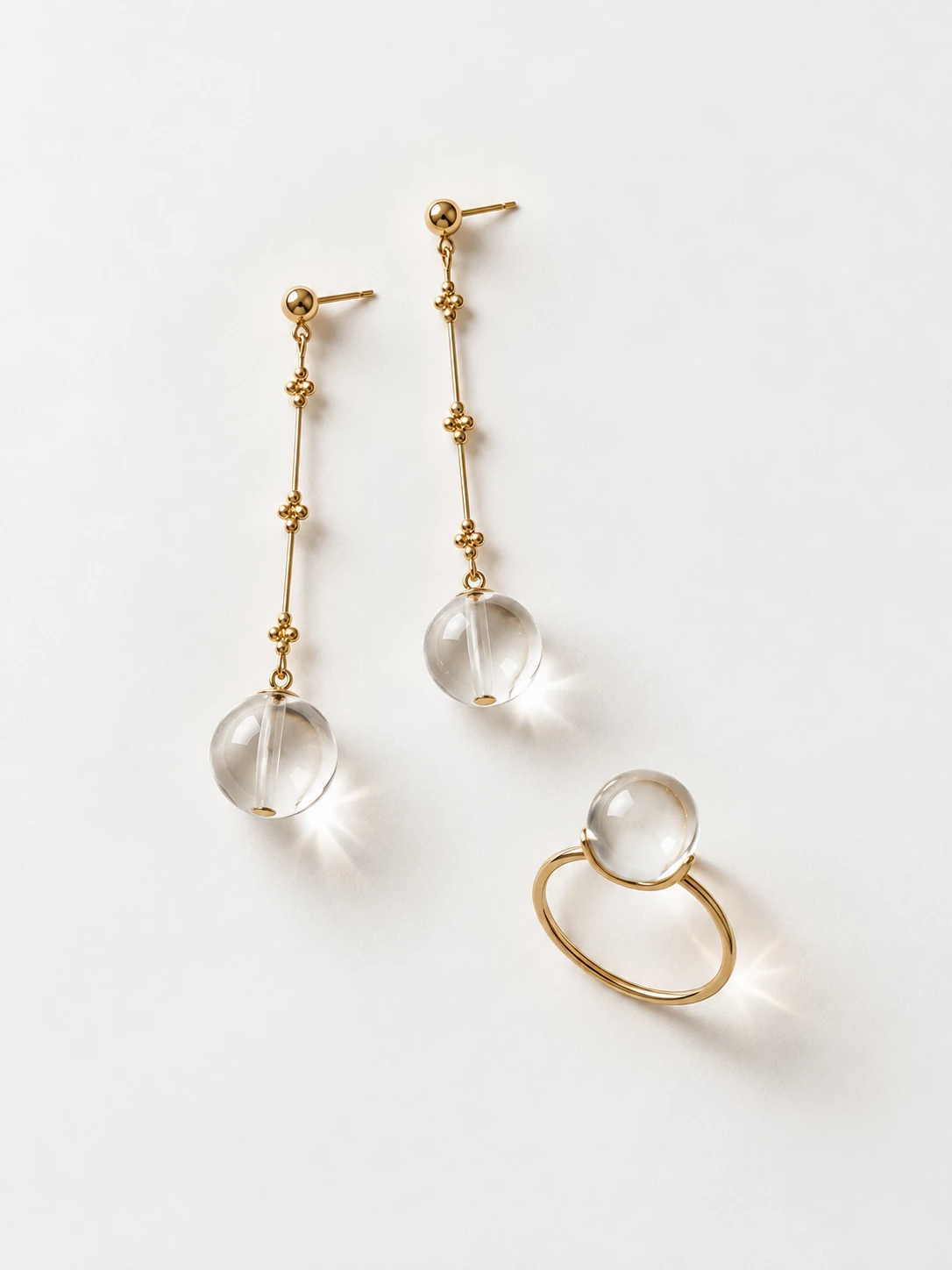 Gold-tone earrings and ring with clear spherical stones arranged on a white surface
