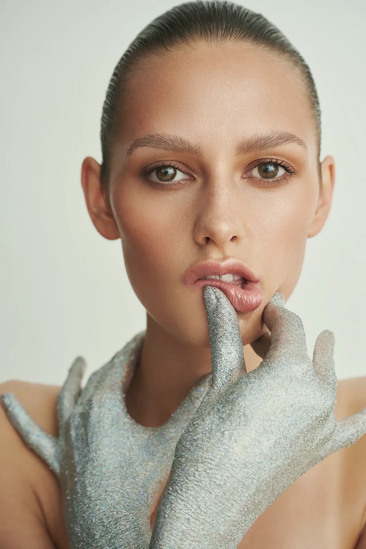 Beauty portrait with silver-painted hand, slicked-back hair and metallic makeup